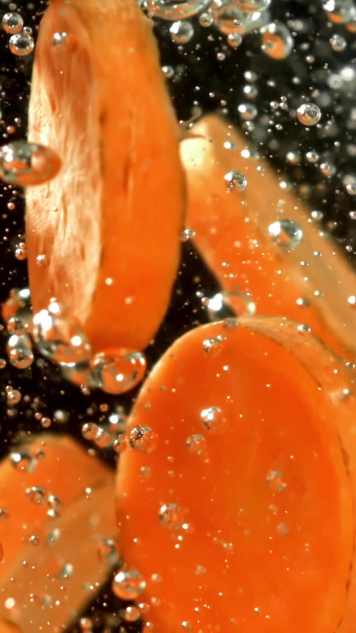Fette di carota fresche che galleggiano in acqua frizzante su sfondo nero