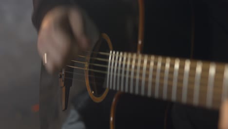 man in a black sweatshirt plays the acoustic guitar