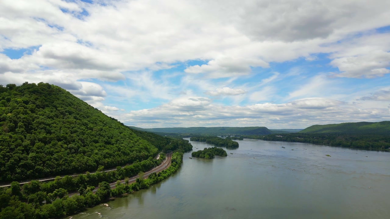 High-altitude drone footage capturing a wide, sweeping view of a large river splitting lush green forested hills and mountain ridges.