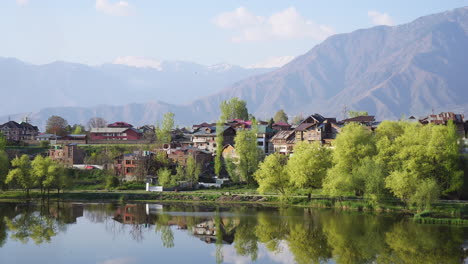 static shot of a peaceful mountain village by a calm lake with scenic snow-capped peaks