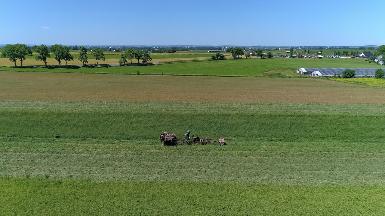 una vista de avión no tripulado de un agricultor amish cosechando su cosecha con cuatro caballos, tirando de un cortador, impulsado por un motor de gas en un día de verano