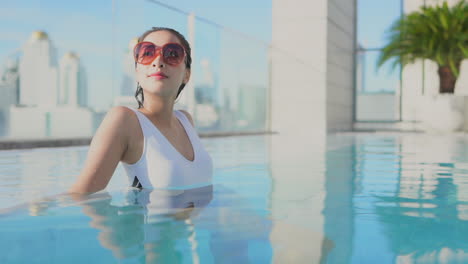 close up of a pretty young woman with an urban skyline in the background relaxes the water of a rooftop swimming pool