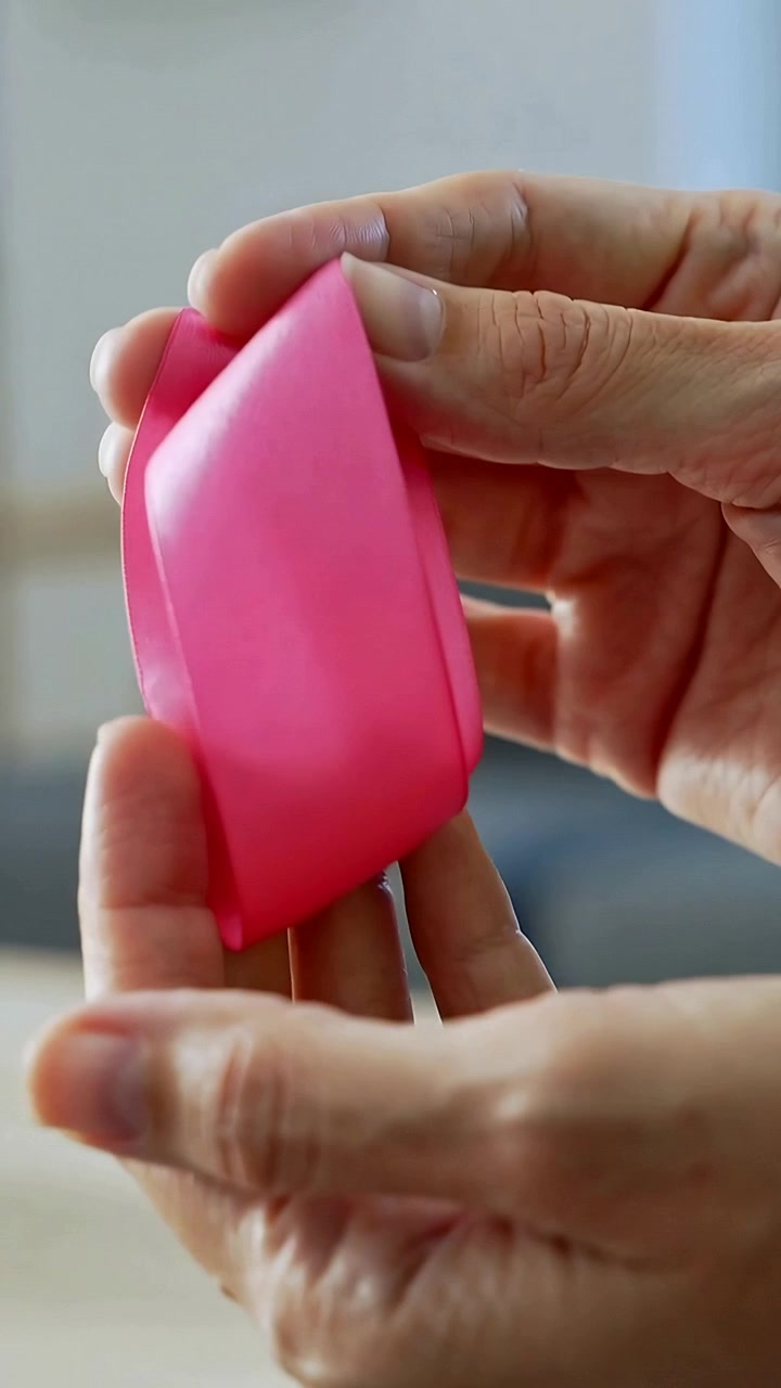 Video verticale: Mani adulte che pizzicano e piegano silicone rosa su un tavolo del soggiorno