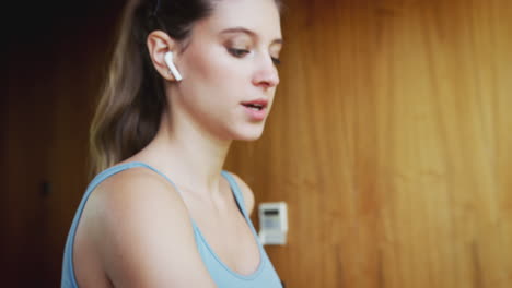 mujer haciendo ejercicio en la cinta de correr en casa usando auriculares inalámbricos comprobando reloj inteligente