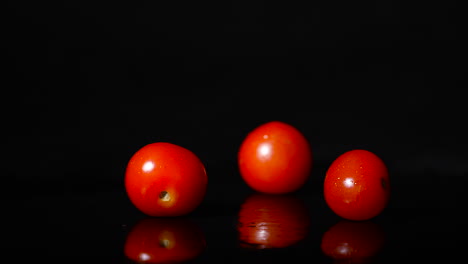vista lateral de tres tomates cayendo en cámara lenta en una superficie reflectante negra