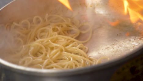 Un-Primer-Plano-De-La-Pasta-Flambeada-Que-Se-Arroja-En-Una-Sartén-A-Cámara-Lenta