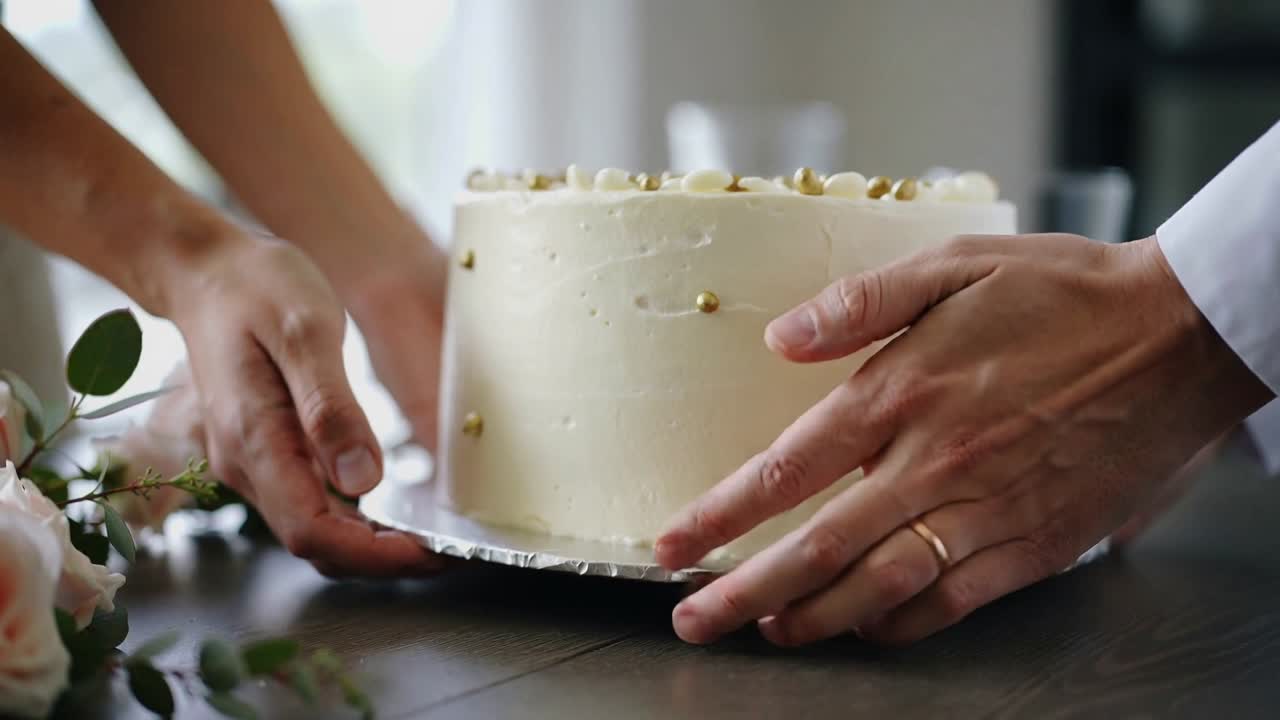自宅でケーキを持つ白い袖のカップルが、ケーキを降ろし、飾るためにグラスの上に置いている。