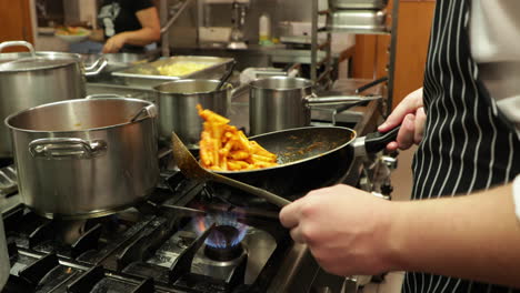 el chef del restaurante lanza pasta penne que se está cocinando en la cocina: cierre, cámara lenta