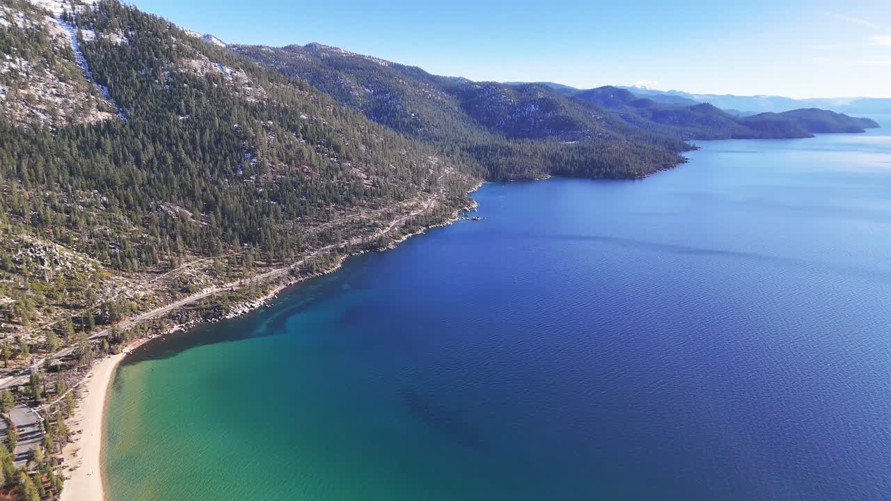 Aerial drone top down view of Sand Harbor State Park featuring white sand beach, clear turquoise water, submerged granite boulders, and pine forest coastline on a sunny summer day