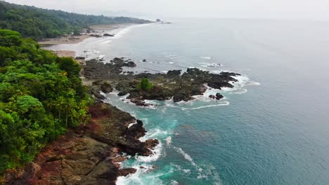 Vista-Aérea-Volando-Sobre-La-Rocosa-Playa-De-La-Selva-De-La-Costa-Pacífica-Con-Olas-De-Agua-Azul-Rompiendo-En-La-Costa-En-América-Del-Sur