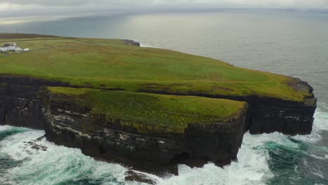 aerial orbit showcases loop head lighthouse, dramatic sea stack, and impressive waves crashing against the cliffs in county clare