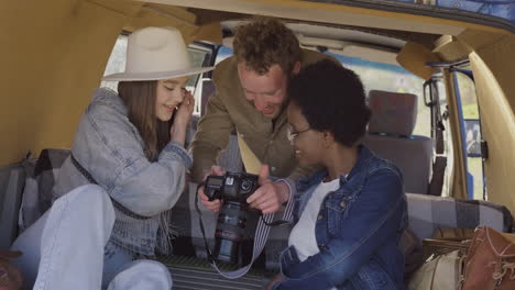 a young photographer shows the pictures he has taken to two beautiful young girls inside the caravan during a roadtrip