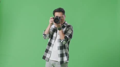 asian photographer taking pictures then looking at them in the camera while standing on green screen background in the studio