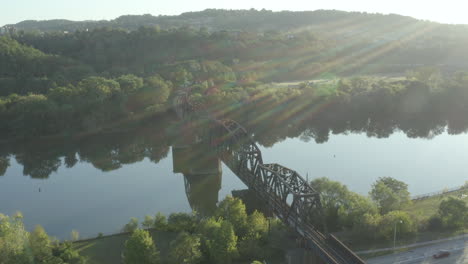 Drone-orbiting-a-rail-bridge-over-water-at-sunrise-with-sun-flares