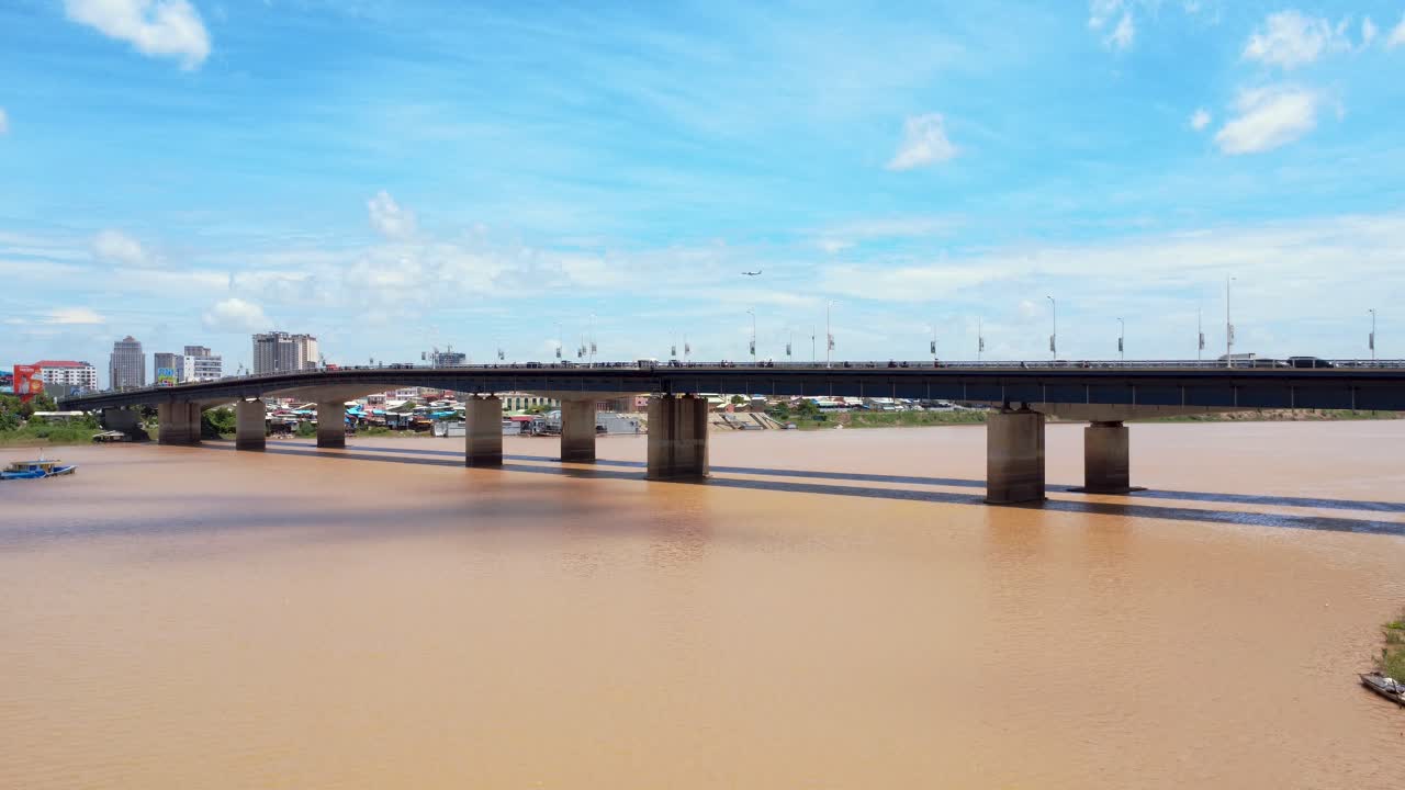 Vibrant aerial footage of Japan Bridge spanning the muddy Mekong River with Phnom Penh's urban skyline under a bright blue sky captures a dynamic cityscape setting, chroy changvar district