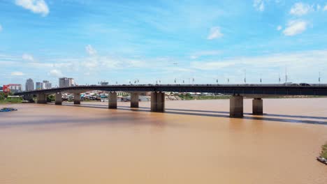 vibrant aerial footage of japan bridge spanning the muddy mekong river with phnom penh's urban skyline under a bright blue sky captures a dynamic cityscape setting, chroy changvar district