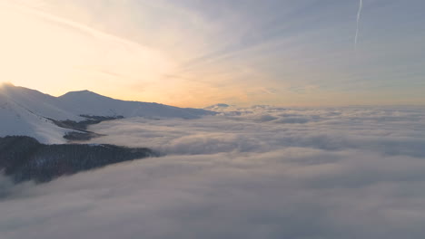 reverse-Aerial-shot,-over-a-clouds,-in-front-of-foggy,-mountain-peaks-and-sunset-colors,-in-the-Balkan-mountains,-on-a-sunny,-winter,-dawn,-in-Central-Balkan-National-Park,-Bulgaria