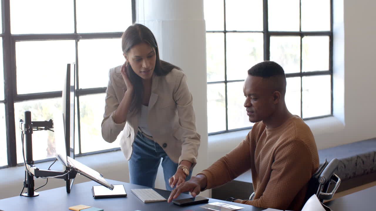 Collaborating in office, colleagues discussing project while using computer at desk