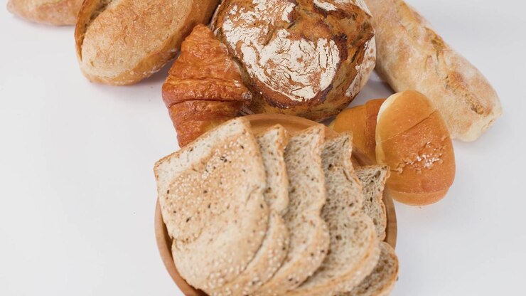 Slow rotating overhead shot of sourdough, croissants, and sliced whole grain bread on white surface.
