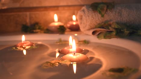 relaxing spa background with candles floating in the bath water, some green petals and a towel near the water surface