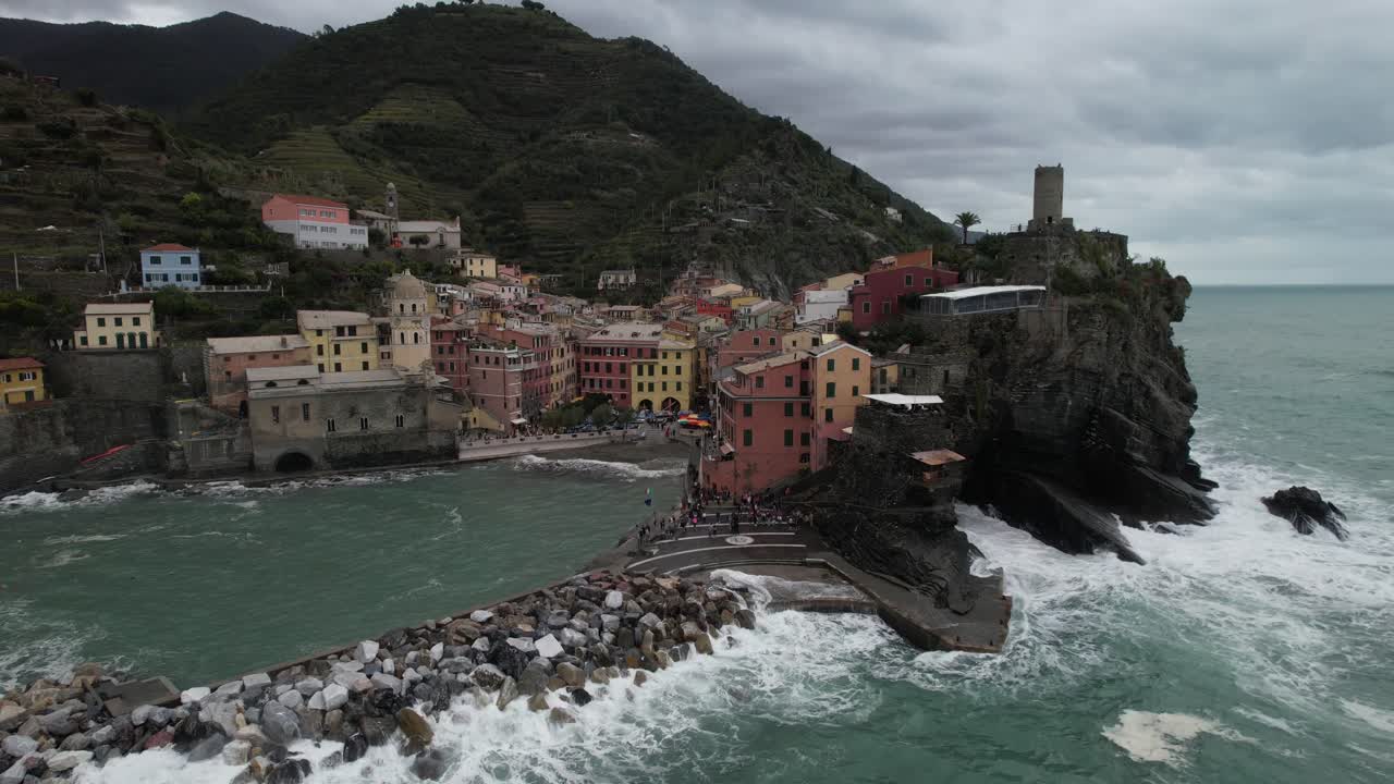 Ripresa orbitale con drone da sinistra a destra del villaggio italiano delle Cinque Terre vicino alla spiaggia, onde che si infrangono, angolazione bassa