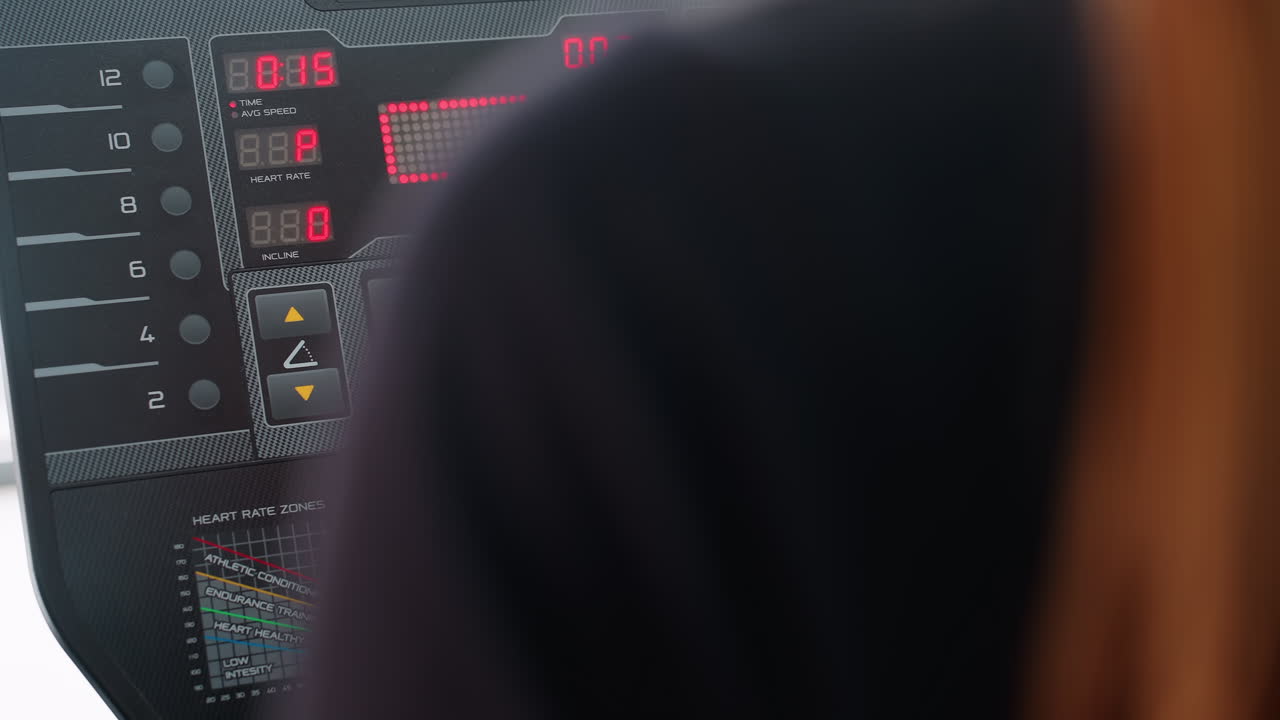 rear view of woman in dark outfit working out on treadmill while adjusting speed setting on electronic control panel with red led display showing workout stats in bright indoor gym environment