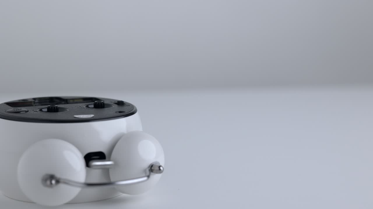 The clock sets the alarm for 6.00 and makes a loud sound to wake it up. Small white alarm clock, hand put the clock down on the table.