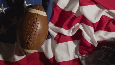 overhead shot of person putting american football onto stars and stripes flag with helmet