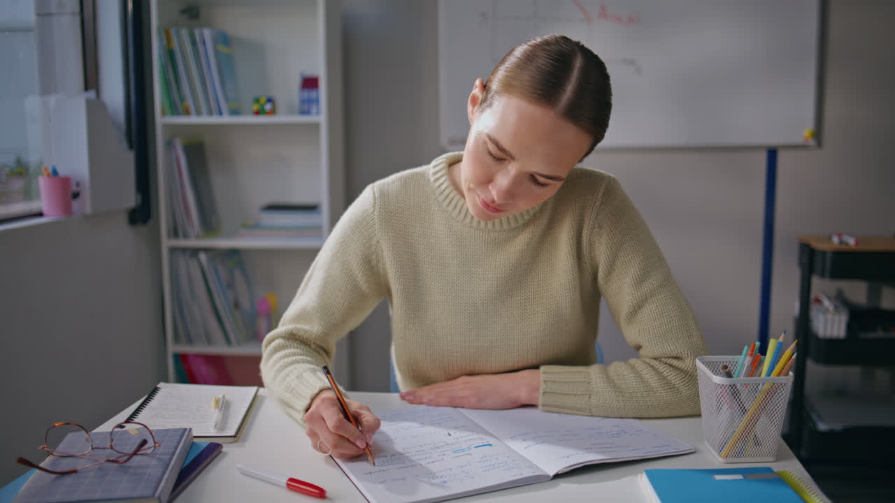 Focused lady checking homework at class room closeup. Teacher putting marks