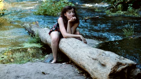 happy and relaxed woman sitting on a tree trunk contemplates nature