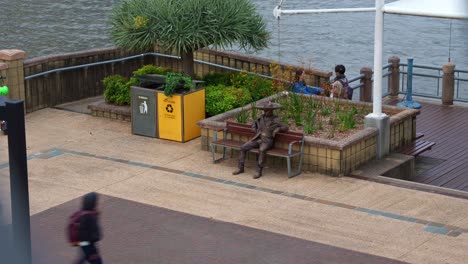 a living statue spotted sitting on the park bench by a riverside promenade in the south bank parklands, brisbane city, time-lapse fast motion shot.