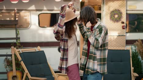 A-happy-brunette-guy-with-a-green-checkered-shirt-dances-A-cheerful-dance-with-his-brunette-girlfriend-in-a-light-brown-shirt-near-their-trailer-in-the-camp-during-a-picnic-and-vacation-outside-the-city-in-the-summer