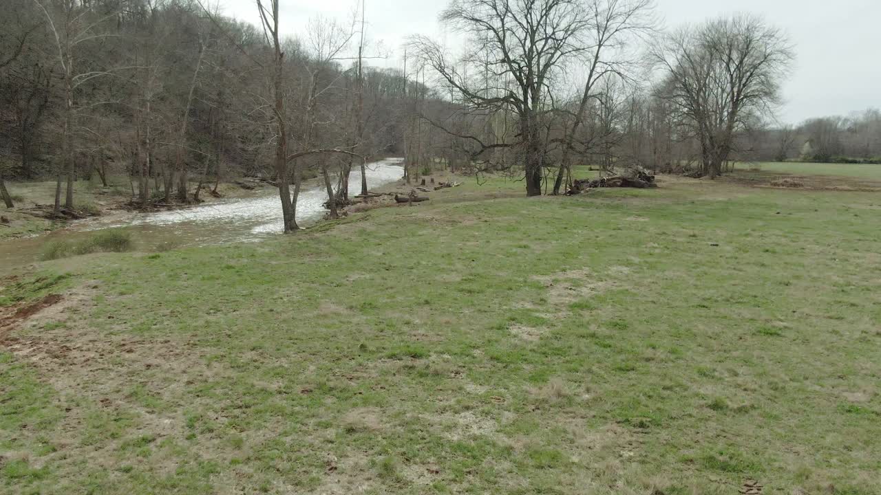 Low altitude aerial beside a river toward a pile of wood to burn