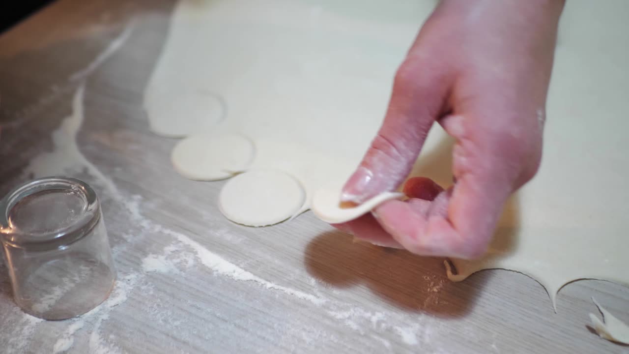 Woman is putting circles of dough for cooking dumplings, hands closeup. Process of cooking dumplings