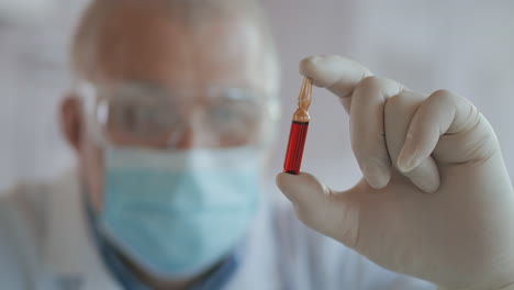 close-up do desenvolvedor da vacina contra o coronavírus segurando uma ampola de líquido vermelho examinando e segurando a vacina em luvas. imagens de alta qualidade em 4k