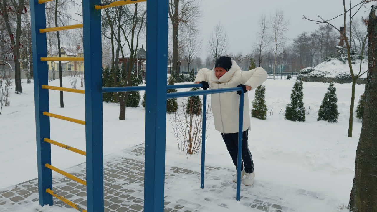 Exercising on the horizontal bar on the sports ground. Aged woman practicing sport in winter.