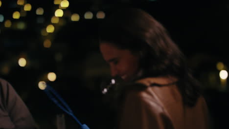 hermosa mujer joven soplando burbujas en su novio en el techo por la noche disfrutando de una noche romántica lúdica con luces de la ciudad bokeh en el fondo