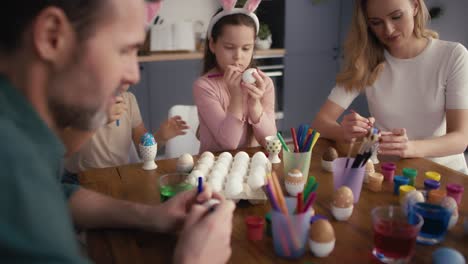 caucasian family of four people decorating easter eggs at home.