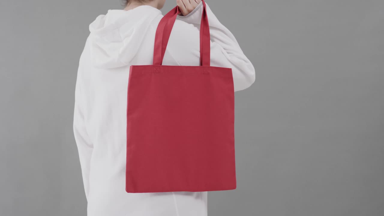 Mujer caucásica con sudadera blanca con capucha sosteniendo una bolsa roja sobre fondo gris, con espacio para texto, en cámara lenta