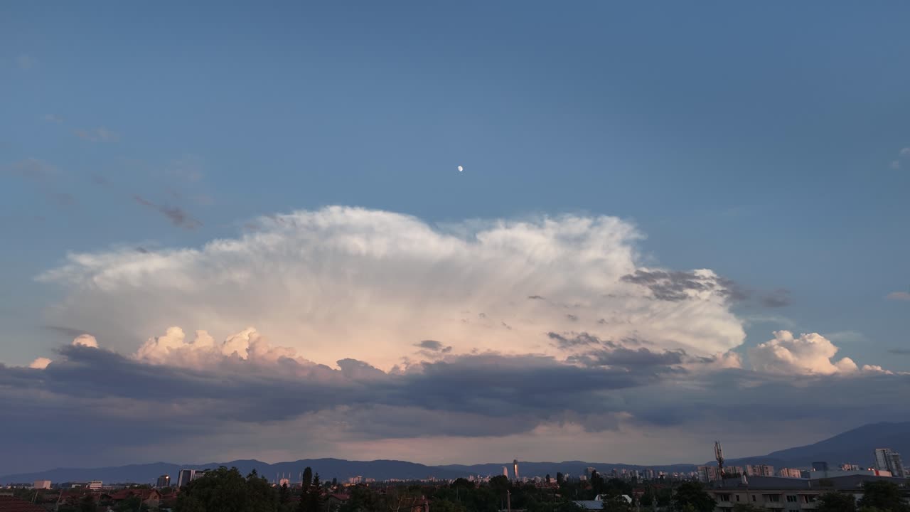 Time Lapse of a Magnificent giant cloud over the city skyline with the moon above it, at dusk. Copy space at the top half of the video. shot in Sofia, Bulgaria