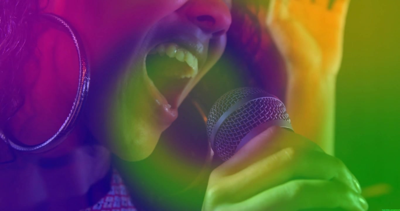 Artista musicale che porta il microfono alle labbra, intensificando la voce per le note più alte mentre le sovrapposizioni di colore pulsano.