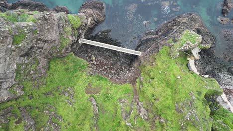 Aerial-birdeye-view-from-the-historic-Gobbins-Cliffs-in-beautiful-Northern-Ireland-overlooking-a-viewing-platform,-rocky-slope-and-rocks-in-the-blue-sea-during-an-adventurous-journey