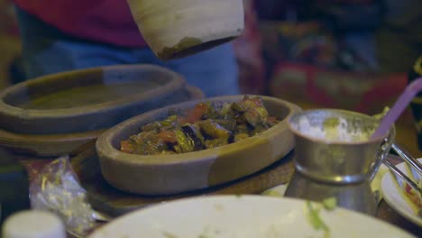 close up of a person serving a meal of meat and vegetables in a clay pot at a restaurant