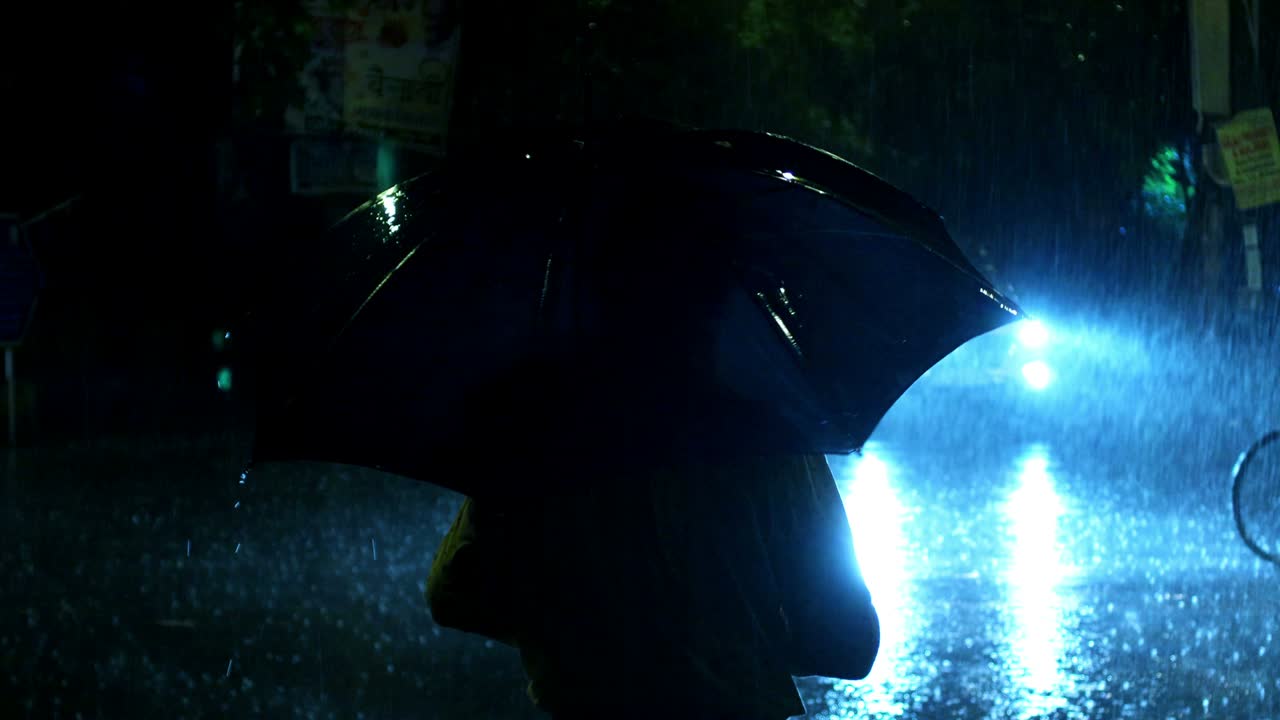 Man spinning umbrella in circular motion while standing on the road in rainy season at night.