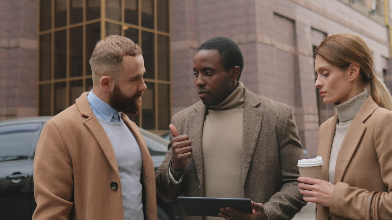 African American businessman holding tablet and giving orders to his colleagues in the street in autumn