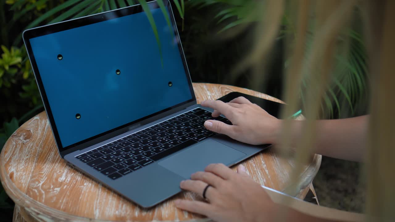 un joven europeo en un vestido azul remotamente en línea trabajando en una computadora portátil con pantalla azul en el patio trasero con plantas verdes