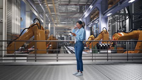 full body side view of asian female with her phone with industrial robotic arms working, she raises her fist up with screaming goal