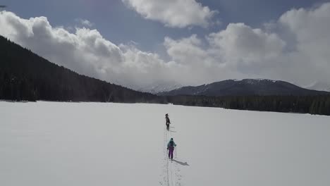 drone shot of backcountry skiers skinning across frozen lake in winter