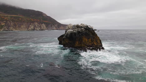 Luftumlaufbewegung-Um-Kleine-Felseninsel-Mit-Meereswellen,-Die-Vor-Big-Sur-Gegen-Sie-Prallen