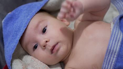 adorable baby lying covered in towel after a bath. sweet boy holding little fist on his chest and waving it from time to time. close up.